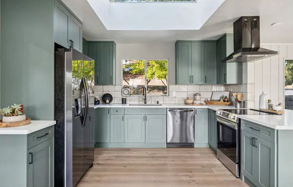 A renovated kitchen with sage shaker cabinetry, quartz counters, and a skylight
